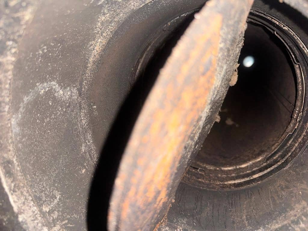 Inside a round metal flue, a rusted damper plate in the foreground and a small point of daylight far up the pipe.